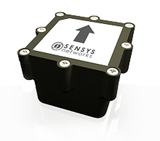 This is a photograph of a magnetometer from Sensys Networks. This device is a cube-like device. At the top of the device is the company logo and an arrow pointing up.