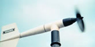 This photograph is an example of an air sensor. This image a wind vane mounted on top of a pole, with a long cylindrical body and a fan to catch the wind on the front and a vertical tail on the back.