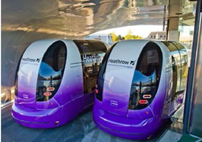 This photo is another example of Personal Rapid Transit (PRT). It shows the recently implemented ULTRA Heathrow Airport Personal Rapid Transit system (PRT). There are two PRT vehicles side-by-side with smooth curved edges, and vertically long tinted windows. The vehicles are purple at the bottom, and gradually fade into white at the top.