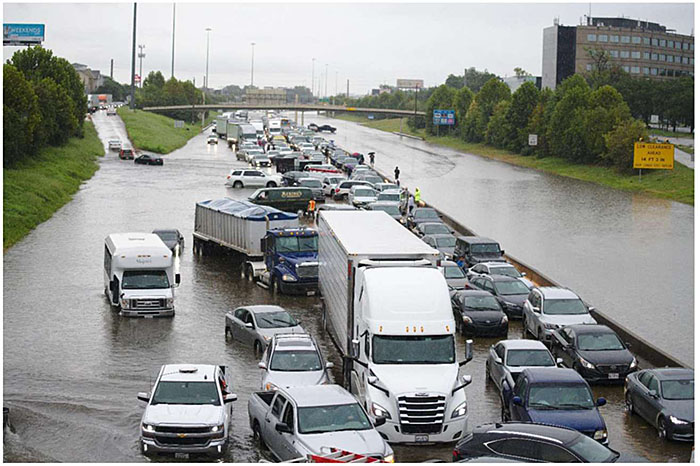 Photo of hurricane flooding in Houston Texas with numerous cars and trucks stuck in standing water on a major roadway, showing an example of complete loss of roadway capacity.