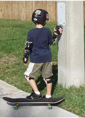A photo shows a young child on a skateboard pressing a crosswalk interrupt button.