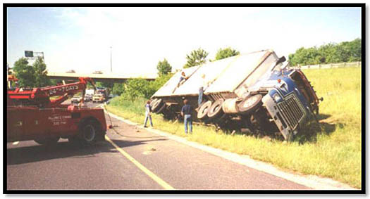 The slide shows a photo of an overturned truck. Please see the Extended Text Description below.