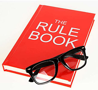 The left side of the slide includes an image of a book entitled “The Rule Book” with glasses sitting on top of it. 