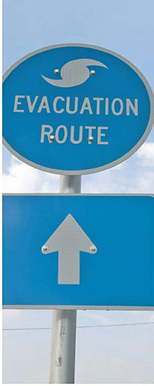 a photo of an evacuation route sign (a round sign with the words Evacuation Route and a symbol of a hurricane, and a rectangular sign underneath with an arrow pointing forward)
