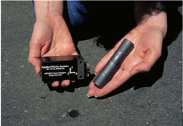 Photo shows a hand holding the magnetometer used on the bus to follow the path created by a series of cylindrical magnets being held in the other hand.