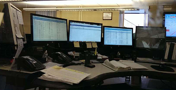 A photo of the Chattanooga Area Regional Transportation Authority (CARTA) dispatch center. The photo consists of three video screens that display dispatch information on a desk where the dispatcher sits.