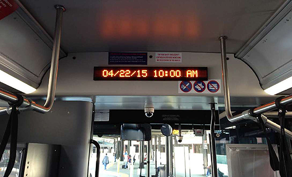 A photo of a dynamic message sign inside a bus located in the front above the driver. The DMS says 4/22/15 10:00AM.