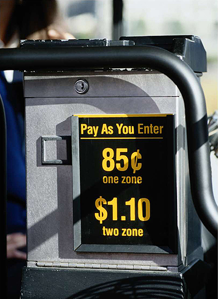 A photo of the side of a fare box that has a sign on it that says: Pay As You Enter: 85 one zone, $1.10 two zones.