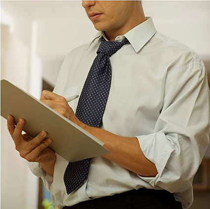 A photo of a man dressed in a tie and button up, holding a pad of paper, and is writing on that pad with a pen. Image Source: thinkstock.com