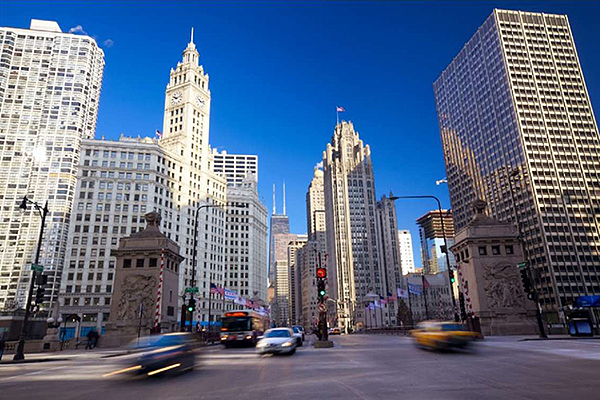 A photograph of downtown Chicago, showing vehicles, a traffic signal pole, and buildings with old architecture. The view is from the street looking up at the sky. The photo was taken during the day. Image Source: thinkstock.com