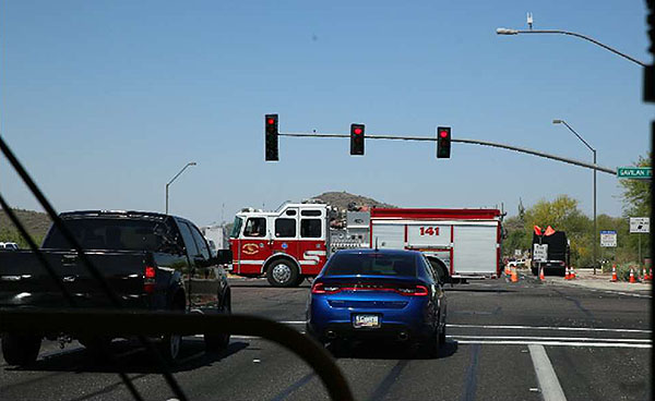 A photo of two vehicle stopped at a signalized intersection, with red traffic signals, as a fire truck crosses the intersection.