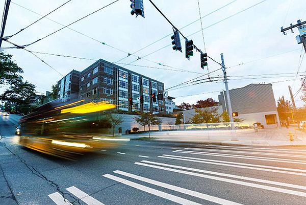 A photograph of an intersection, with four traffic signal heads and a transit vehicle. The bus was captured while moving and shows a motion blur following it, which makes the bus look like it was traveling at a high velocity. Image Source: thinkstock.com