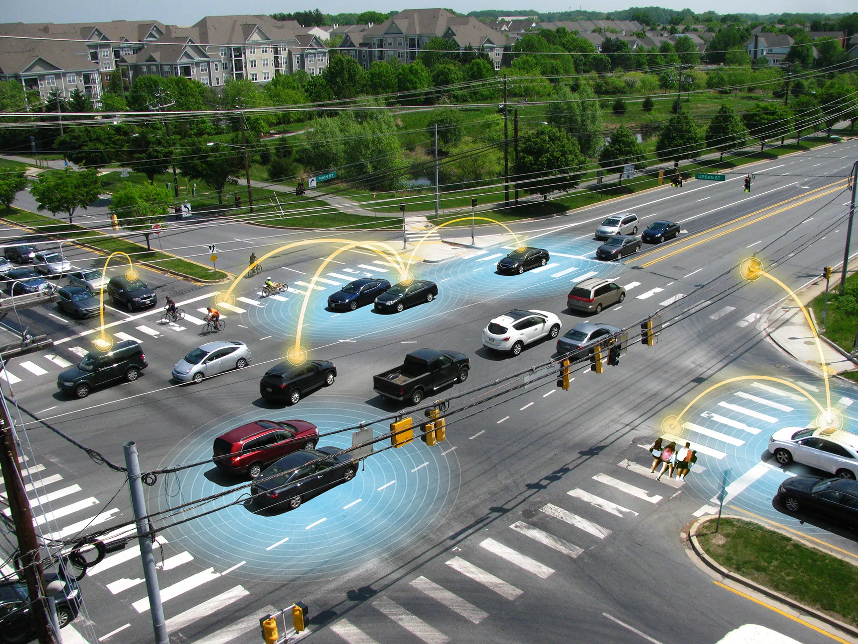 Aerial view of a busy intersection with multiple vehicles and pedestrians highlighted by blue detection zones and golden communication nodes, demonstrating vehicle-to-everything (V2X) communication infrastructure and detection capabilities.