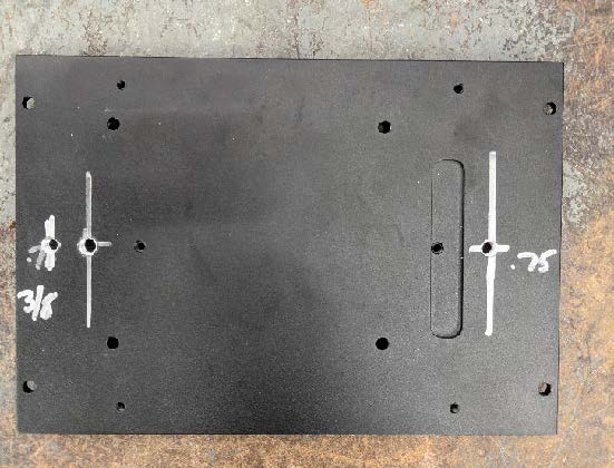 This photo demonstrates the correct placement of holes on the bottom plate of the NUC computer. The left hole is labeled three-eighths of an inch from the left edge and the right hole is labeled three-fourths of an inch from the right edge.