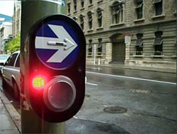 photo of a yellow light next to a speaker and below a raised right-facing arrow on a pedestrian crossing sign