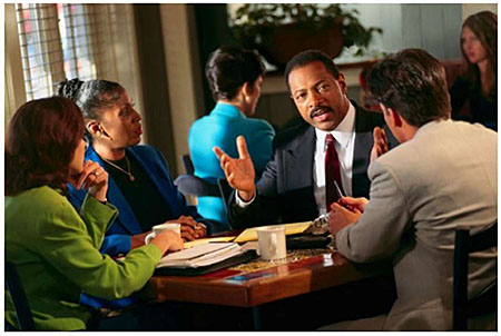Photo of four individuals dressed in business attire having a business meeting while seated at a table.